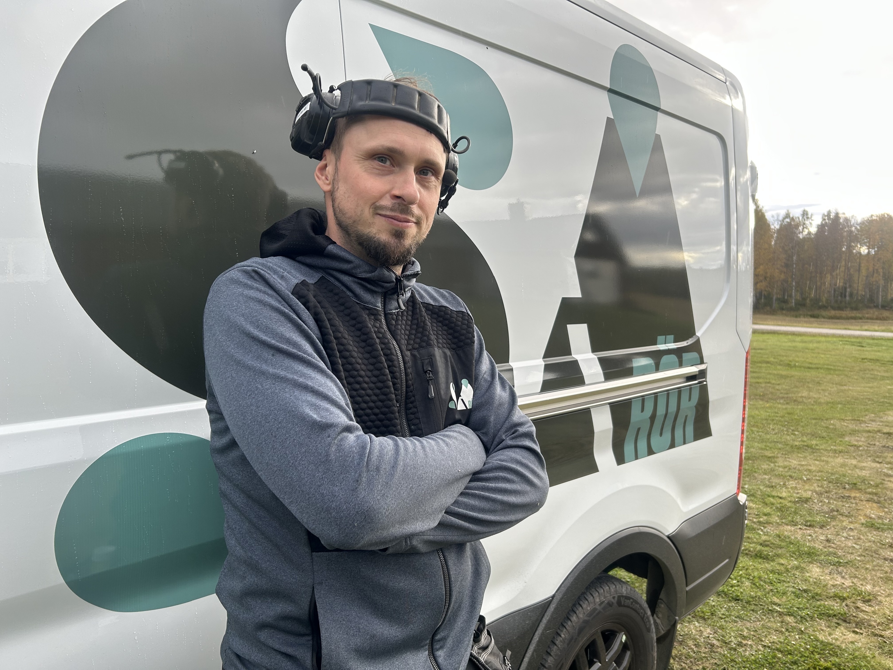 En rörmokare lutar sig mot sin firmabil med armarna i kors och med hörselkåpor på huvudet